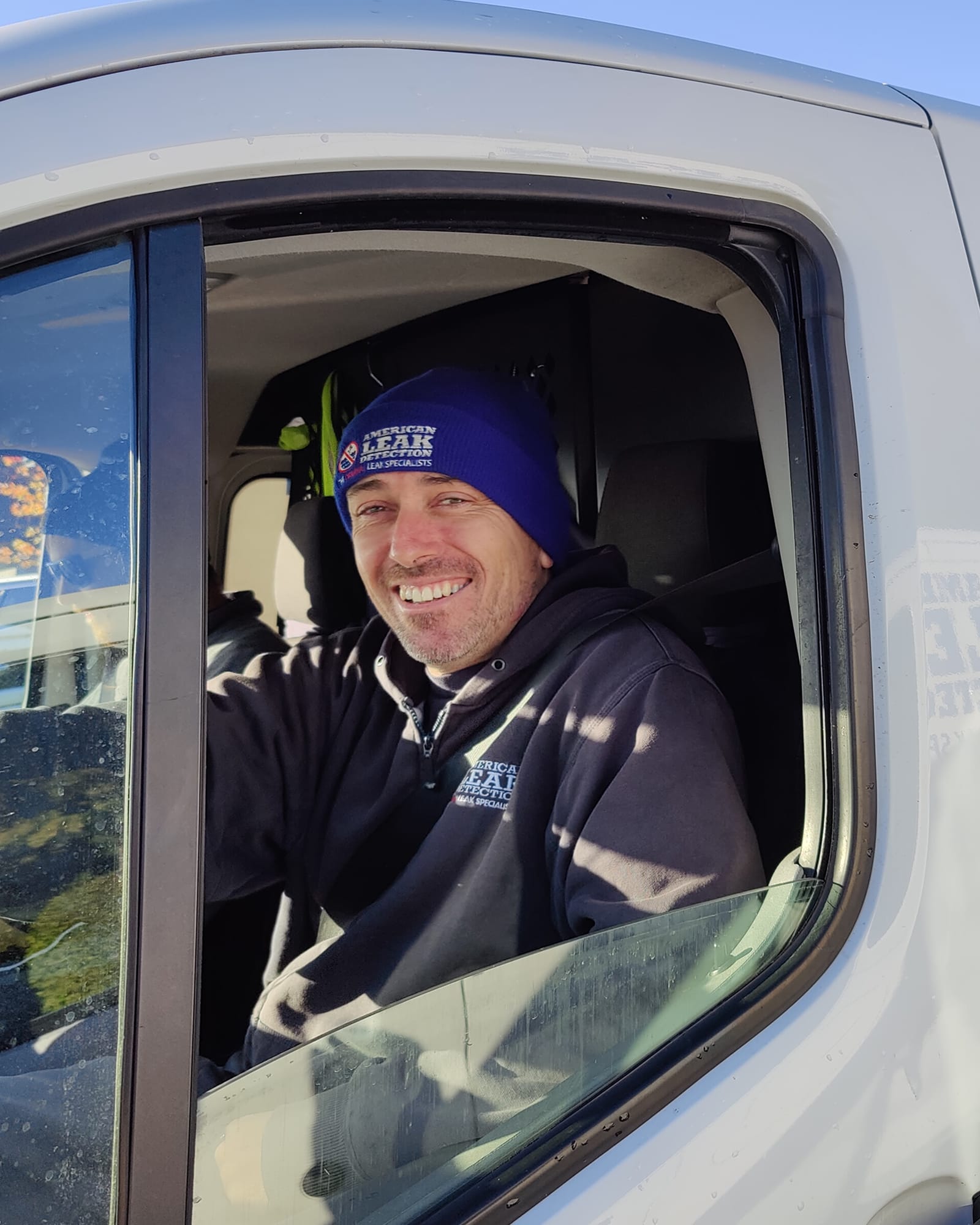 American Leak Detection technician seated in a service van wearing branded work gear.